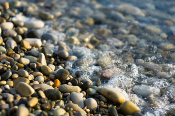 pebble stones on the sea beach, the rolling waves of the sea with foam