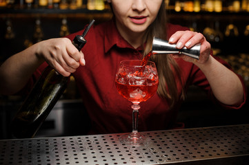 Woman barman pouring bitter into a glass for making an Aperol syringe cocktail