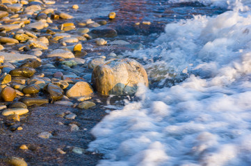 pebble stones on the sea beach, the rolling waves of the sea with foam