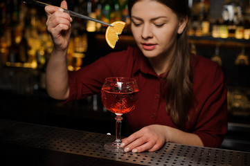 Female barman putting a slice of orange into a glass of Aperol syringe cocktail