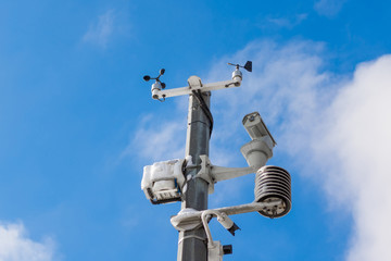 Automatic weather station, with a weather monitoring system and video cameras for observation. Against the background of a blue sky with clouds. - obrazy, fototapety, plakaty