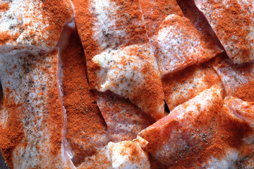 Many raw sliced fresh fish fillets pink pieces well sprinkled with red pepper, are ready for baking top view closeup