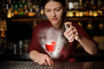 Beautiful woman barman sprinkling a cocktail glass filled with tasty Aperol syringe summer cocktail with a peated whisky