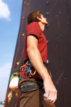 Close-up detail of rock climber wearing safety harness and climbing equipment outdoor wich chalk magnesium bag and carabiners. Artificial training climbing wall on background. Man prepares for workout