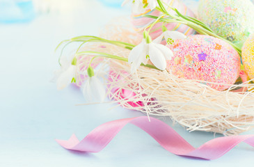Easter colorful eggs background. Beautiful colorful eggs with decorations over blue wooden background, border design in pastel colors. Spring flowers, holiday ribbon and painter eggs in the nest