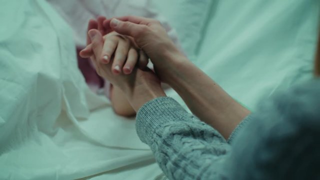Mother Takes and Holds Hand of Her Sick Little Girl who Is Sleeping in the Hospital Bed. Sad and Hopeful Emotional Moment in Pediatric Ward. Shot on RED EPIC-W 8K Helium Cinema Camera.