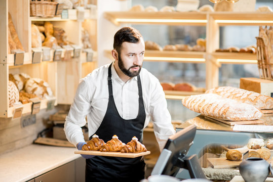 Handsome bread seller with croissants in the small and cozy store with bakery products