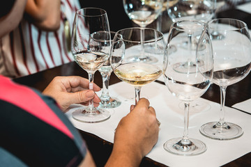 woman holds two glasses of white wine. people consider the color of the wine and try how it smells in different glasses
