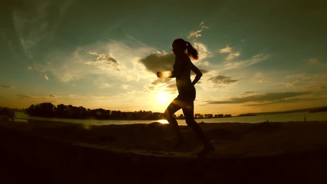 Young attractive woman is running in park at sunset, slow-motion, silhouette