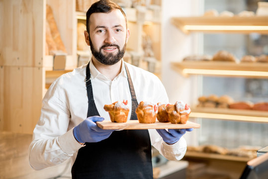 Portrait of a handsome seller with maffins in the beautiful store with bakery products