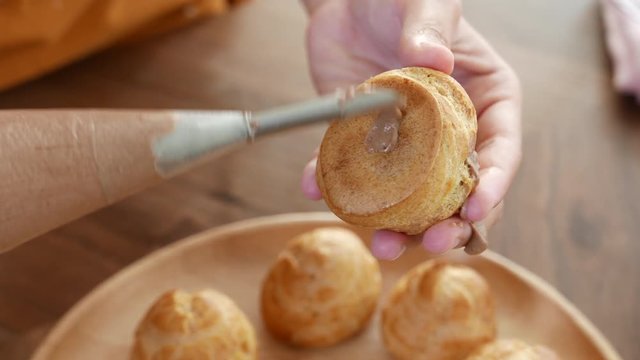Bakery pastry chef filling cream inside cream puff or profiterole or choux creme.