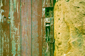 Part of the door with a peeled red paint. Part of the stone wall.
