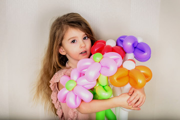 brown-eyed little girl hugs a bouquet of flowers from inflatable balls of red, orange, pink and lilac with both hands 2