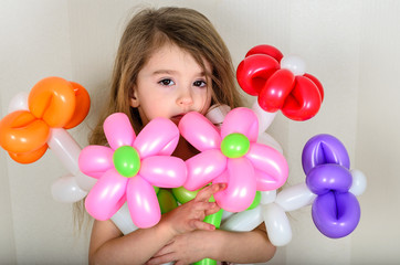 Fototapeta na wymiar brown-eyed little girl hugs a bouquet of flowers from inflatable balls of red, orange, pink and lilac with both hands 3