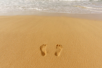 pair of footprints in the sand and sea surf