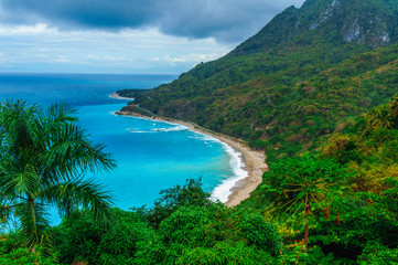 Obraz premium juicy natural wild landscape with rocky mountains overgrown dense green jungle tree, palm and clear azure water of sea ocean