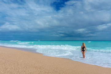 Fototapeta na wymiar beautiful blonde girl in a black swimwear walking on an empty Caribbean beach