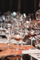 woman holds glass of red wine. people consider the color of the wine and try how it smells in different glasses