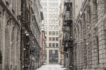 Street Alley of Old-Montreal in winter under a snow storm with a modern skyscraper in the...