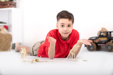 the boy the brunette in a red t-shirt  on a floor plays with toy skeletons of dinosaurs.
