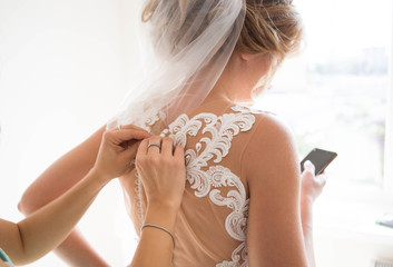 bridesmaid hands fastens buttons on the back of the bride on the wedding dress with beige corset...
