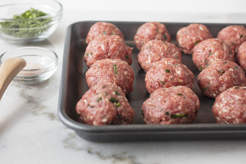 Raw meat balls prepared and ready to be baked on a sheet pan with seasonings on the side