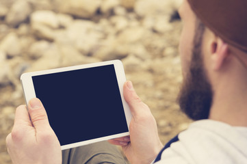 Close-up of a horde in a brown cap in the open air holds a white tablet pc in his hands. A bearded man looks at the tablet. OTS view from behind the shoulder