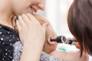 Doctor examining childs ear with otoscope. Mom holding baby with hands. Children healthcare and...