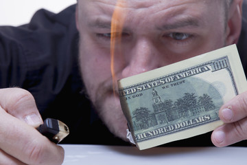 Money is not the best method of employee motivation. Close up a man burns a hundred dollar bill.