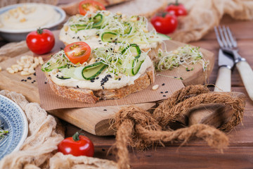 Healthy vegetarian bruschettas with bread, micro greens, hummus, cherry tomatoes, cucumbers and pine nuts
