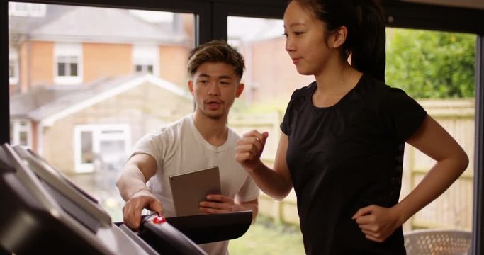 4K Personal trainer with digital tablet mentoring young woman working out on treadmill