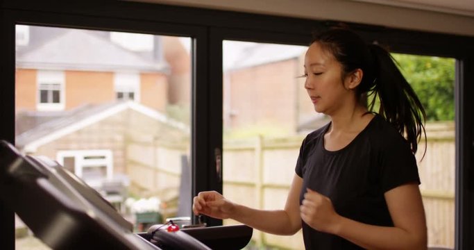 4K Young fit Asian woman running on treadmill in home gym. Slow motion.