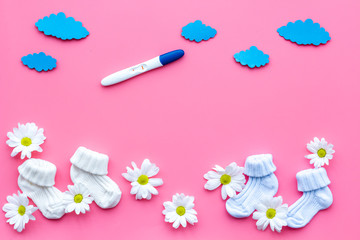 Pregnancy test, socks and flowers pink background top view mock up