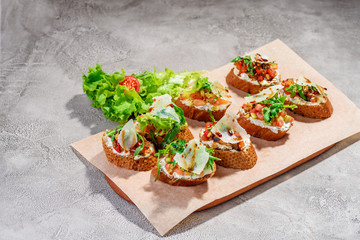 Italian bruschetta with salmon, tomatoes, cheese and basil pesto on a grey concrete or stone background.
