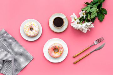 woman desk with flowers, coffee and donuts for breakfast in spring desing pink background flat lay
