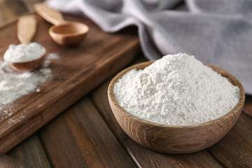 Fototapeta na wymiar Wheat flour in bowl on wooden table