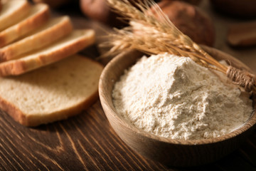 Fototapeta na wymiar Bowl with flour and wheat spikes on table. Baking bread