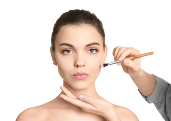 Visage artist applying makeup on woman's face against white background. Professional cosmetic products