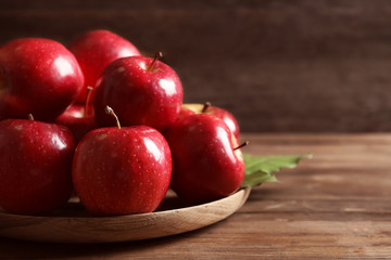Plate with fresh ripe red apples on wooden table
