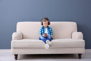 Cute little boy listening to music on sofa, indoors