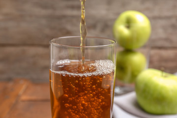 Pouring fresh apple juice into glass on wooden background, closeup