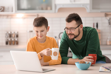 Little boy and his dad using laptop in kitchen