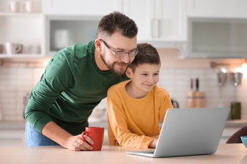 Little boy and his dad using laptop in kitchen