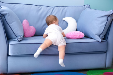Cute baby climbing on couch in living room
