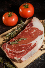 Raw ribeye steak with a sprig of rosemary, garlic and tomatoes