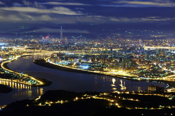 Fototapeta na wymiar Aerial panorama of Taipei City in a blue gloomy night, with view of Kuandu plain, Tamsui River, downtown area and Taipei 101 tower in XinYi District, in evening twilight
