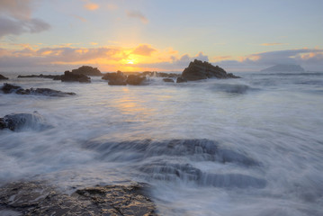 Golden rays of the rising sun light up the rocky beach at Wai'ao, Yilan, Taiwan (Long Exposure Effect)~ Scenery of a beautiful beach illuminated by the first rays of morning sunshine at Ilan, Taiwan  