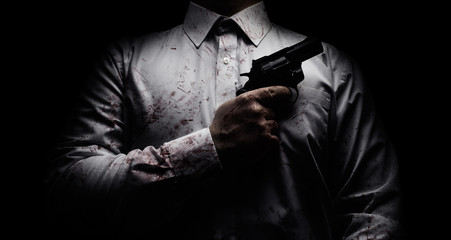 Fototapeta Horror scary photo of a killer in white shirt with blood splatter and posing with black gun on dark background. obraz