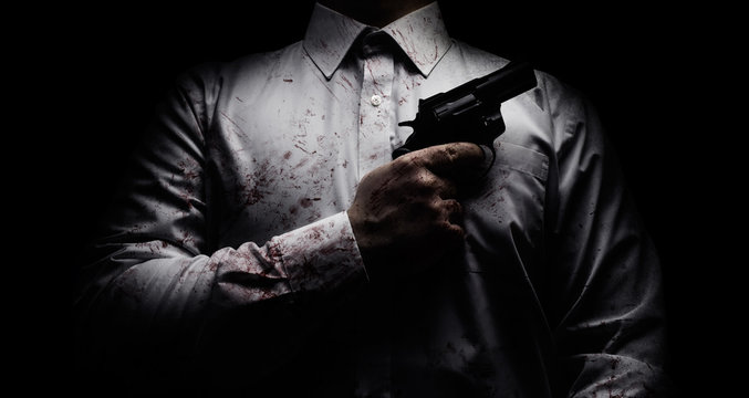 Horror scary photo of a killer in white shirt with blood splatter and posing with black gun on dark background.