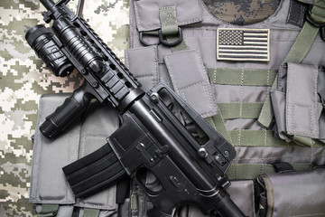 Upper view photo of a military bulletproof vest with american flag badge and rifle laying on a...